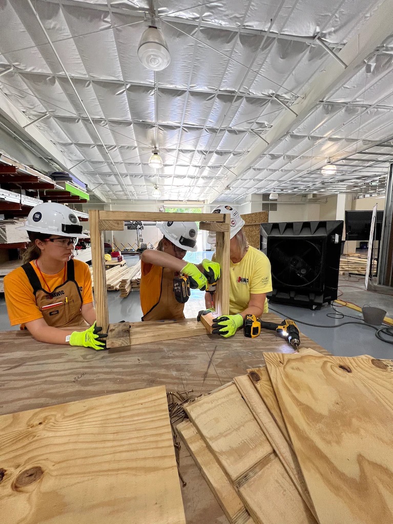 Ainsley Muller, middle, assembles the frame for a doghouse in July with Madison Ancira, left, and instructor Cathy Schernik